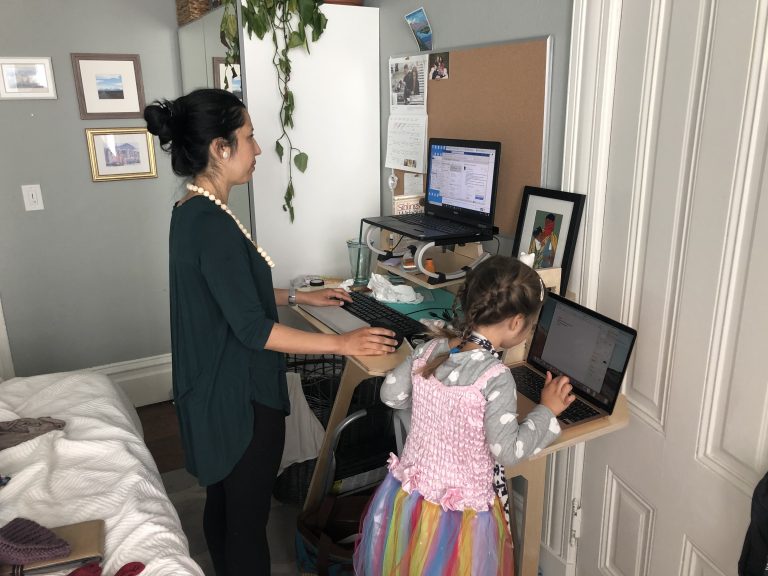 adult working from a stand up desk with a child working on a laptop next to them