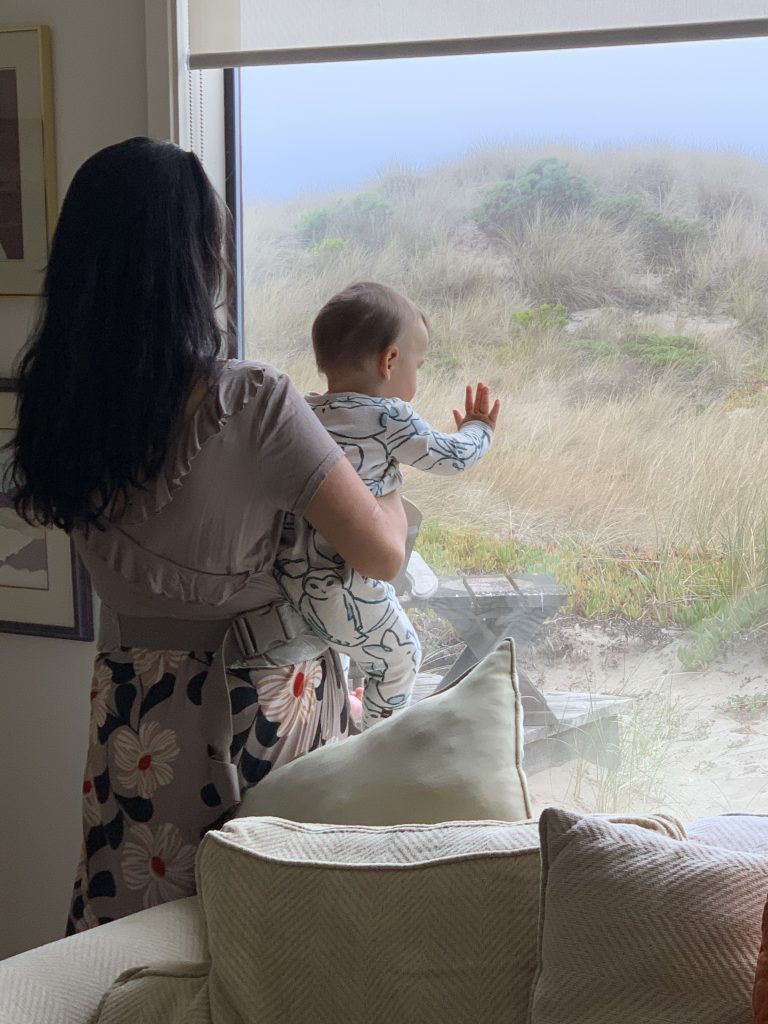 Adult holding a baby looking out the window at sand dunes.