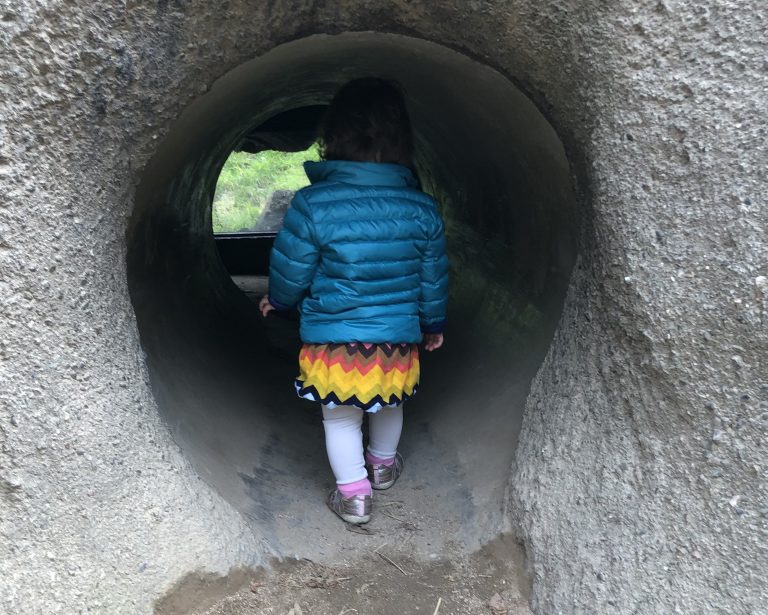 child entering a dark tunnel wearing a teal puffy coat