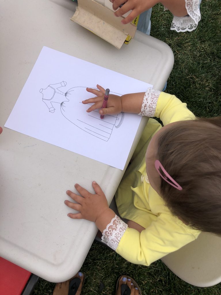 child in a yellow dress coloring an image of a dress from the play Hamilton.
