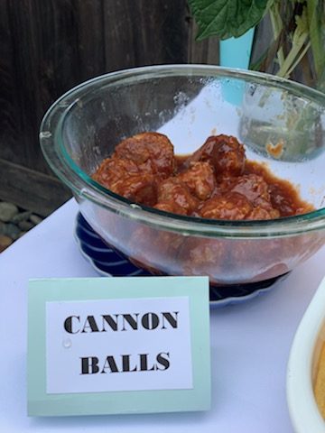 A glass bowl full of meatballs behind a sign that says 