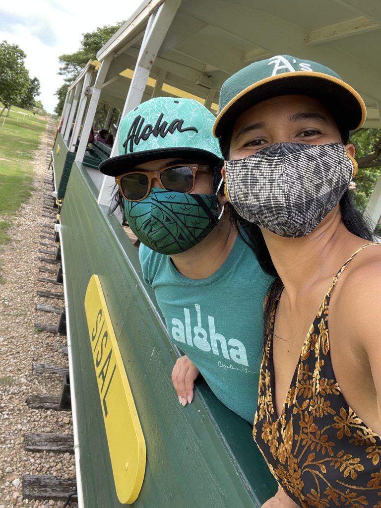 Jelly and her partner (both masked), smile at the camera while riding a green train named "Sisal."