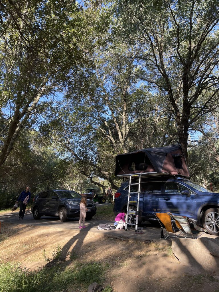 Two cars (one with a tent atop it) are parked under trees at Folsom State Recreation Area. Two children can be seen in the foreground.