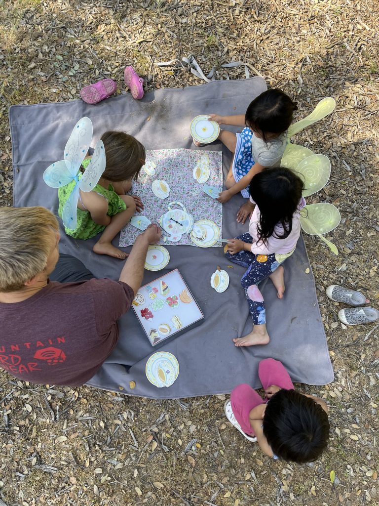 A bird's eye view shot of children wearing fairy wings and playing the Tea Party board game with a dad.