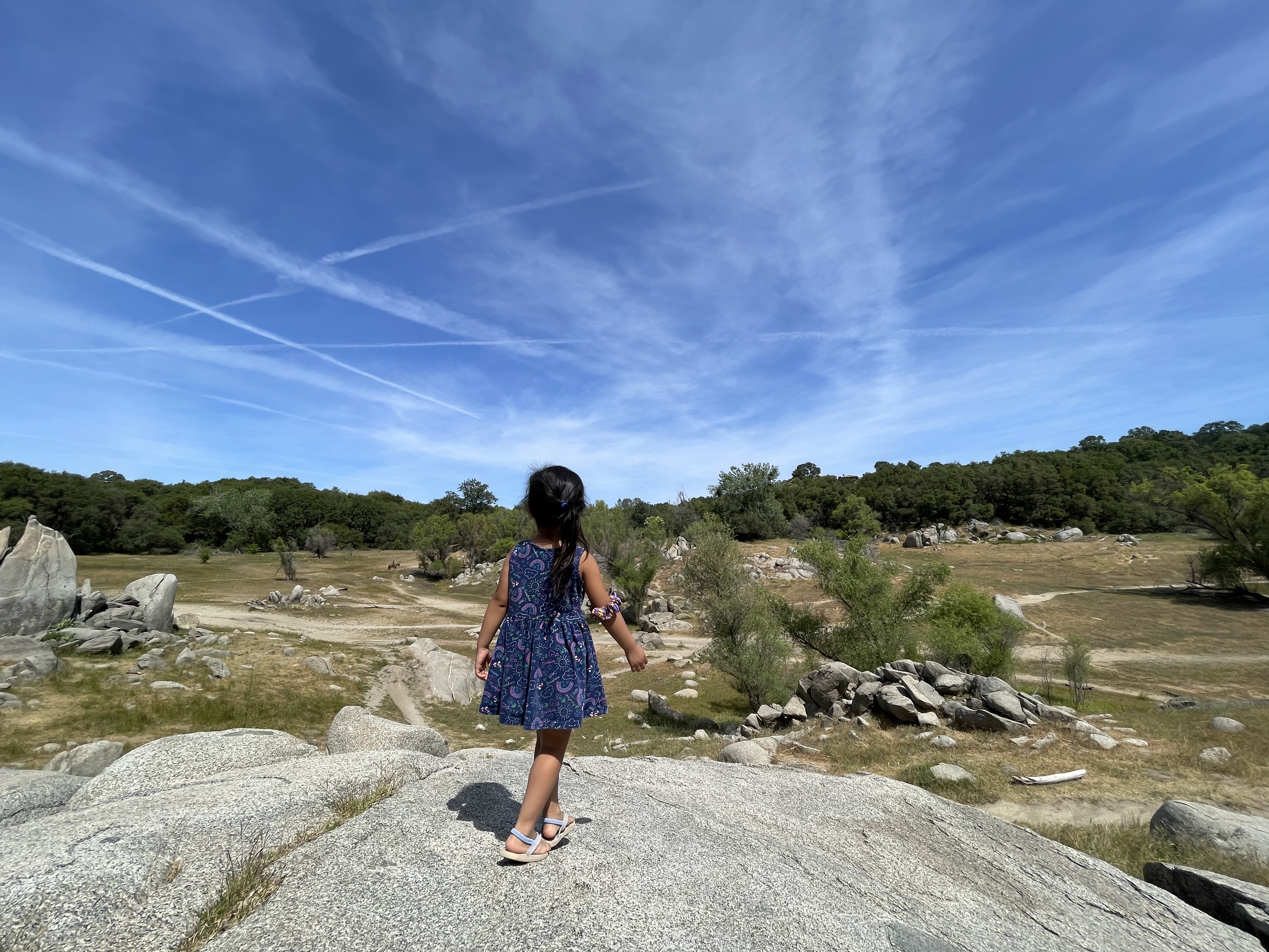 A child stands atop one of the crags found at Beeks Bight, with a hazy blue sky in the background.