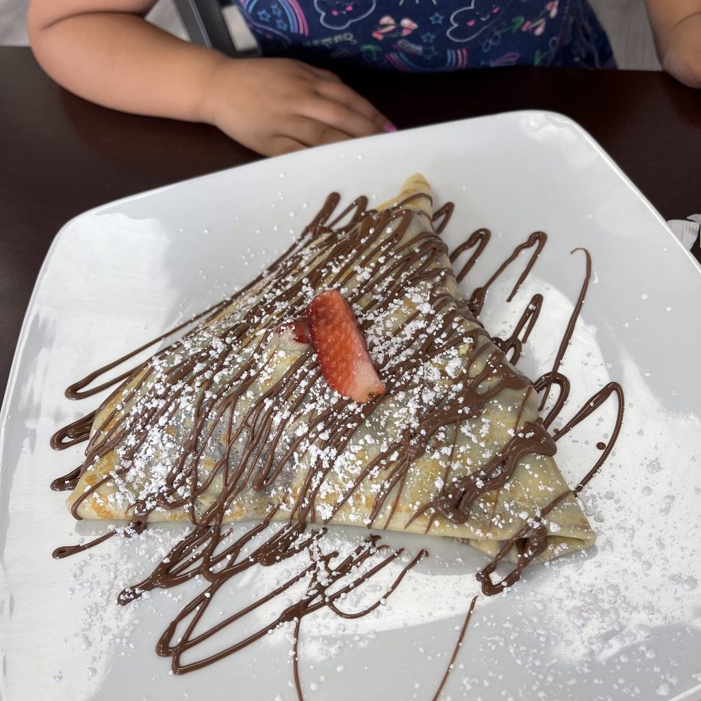 A photo of a triangular crepe topped with chocolate drizzles, powdered sugar, and a single strawberry slice.