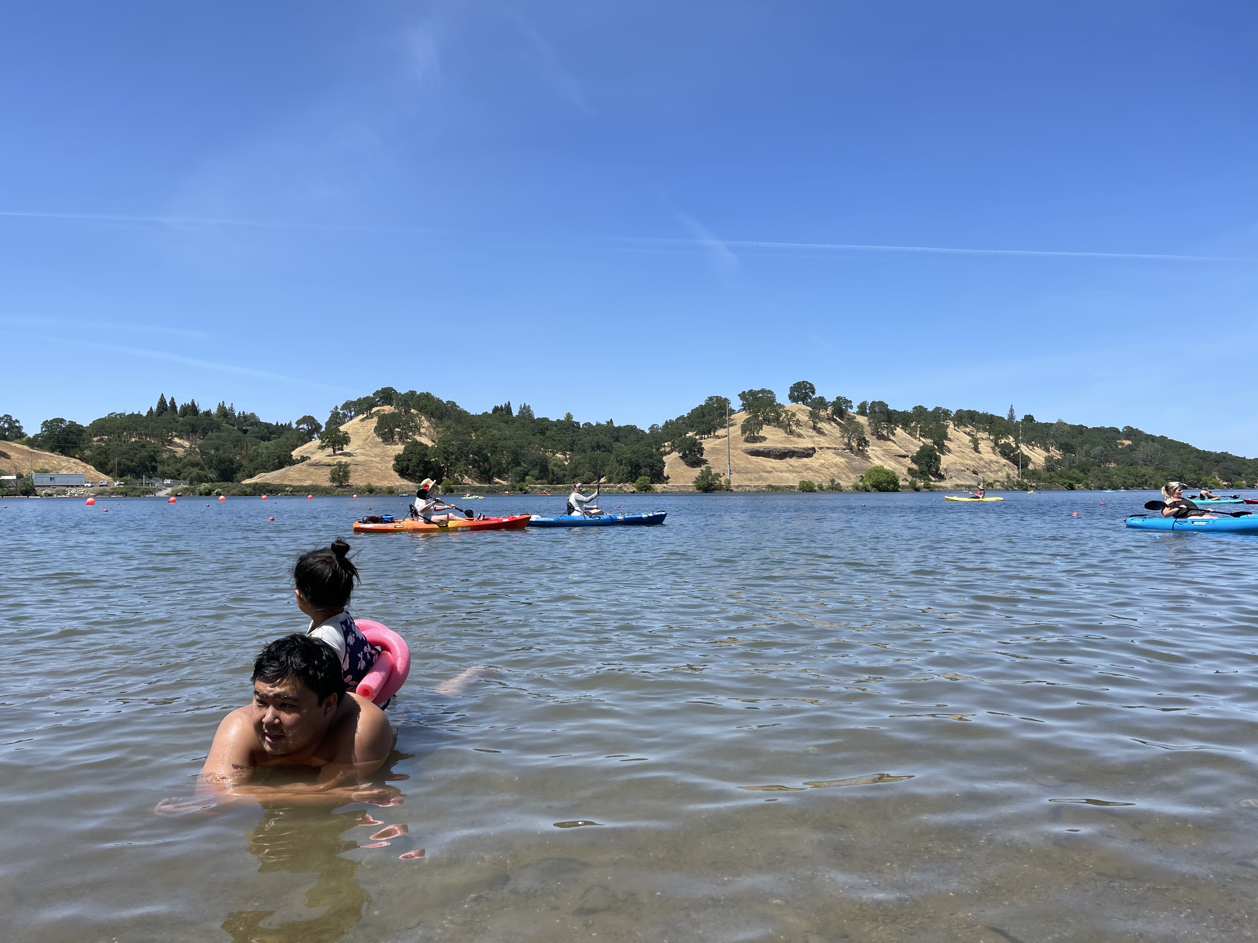A Dad and his child are playing in the water with kayakers and rolling hills in the background at Nimbus Flats.