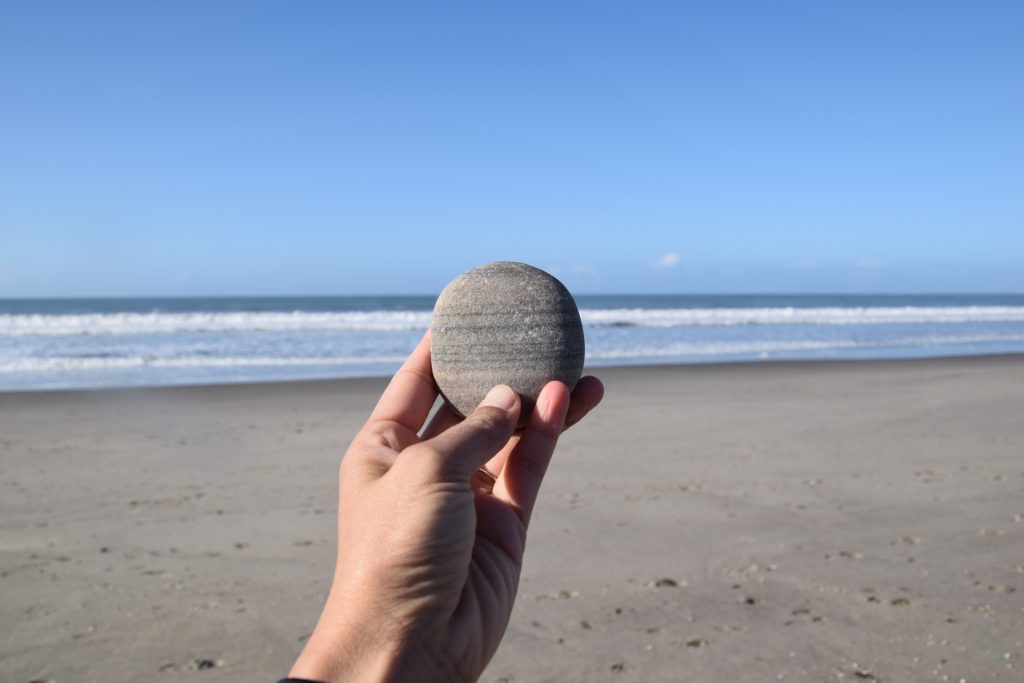 hand holding a striped beach rock with the ocean behind