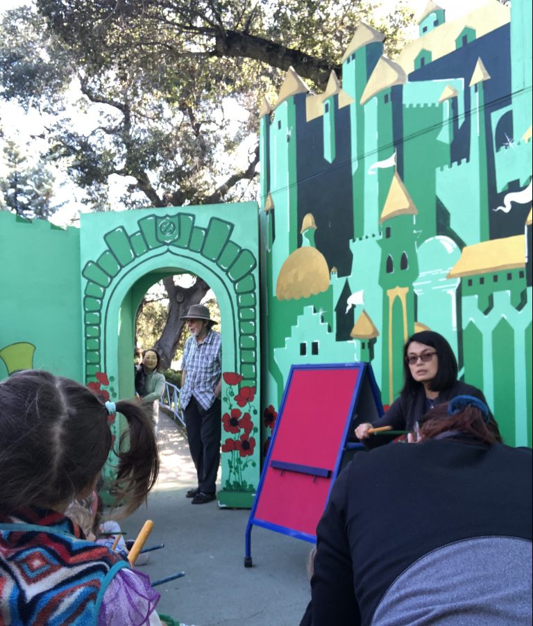 Person telling a story at in front of a painted Emerald City backdrop.