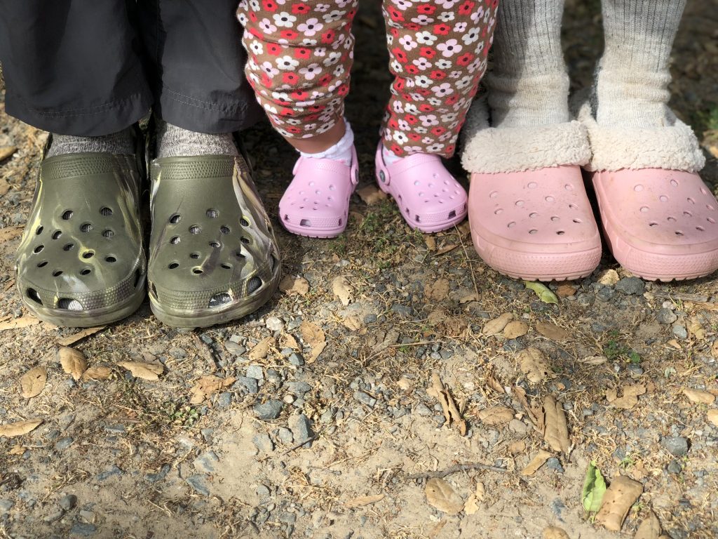 three pairs of feet wearing crocs in the dirt