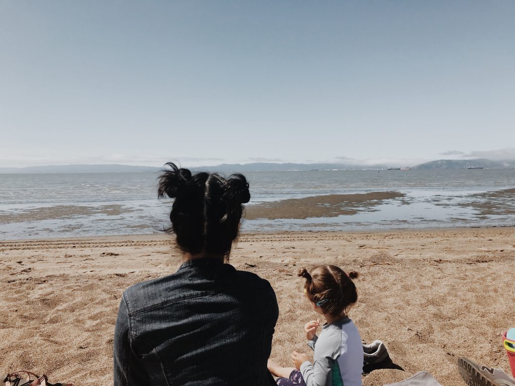 parent with matching hair buns with little kid staring at the ocean