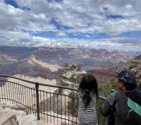 A small child and her father face away from the camera to look out at the Grand Canyon in the distance.