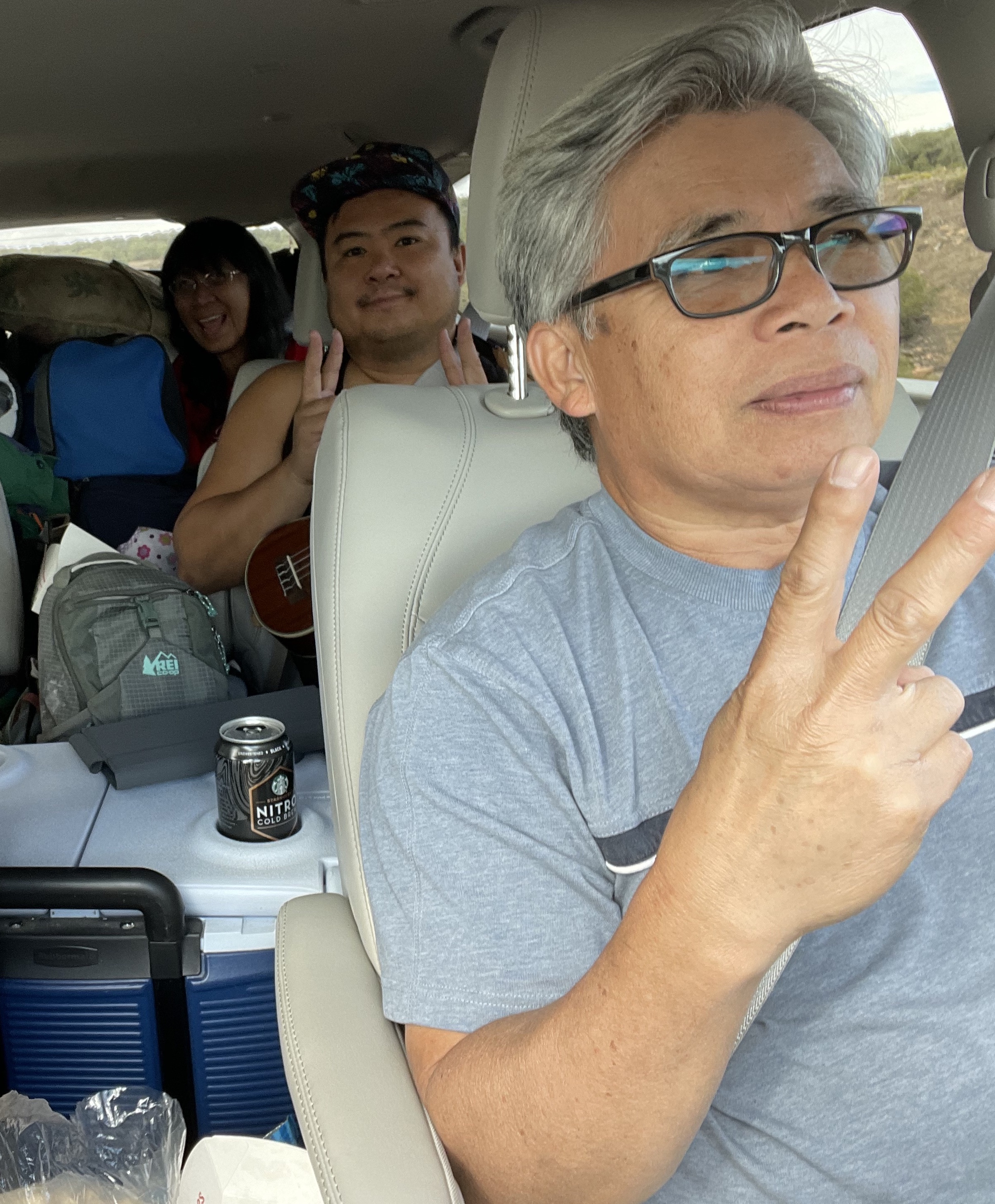Three adults smile for the camera from the inside of a minivan packed with roadtrip gear.
