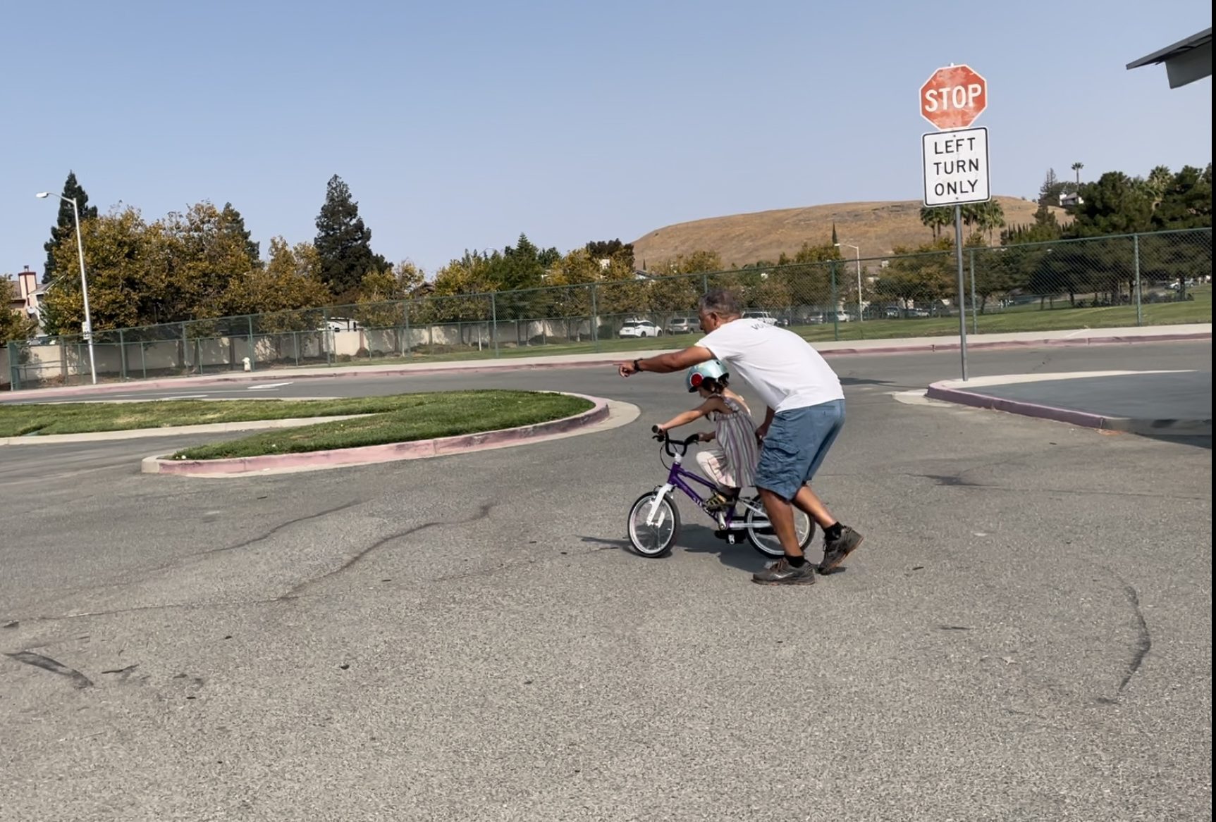 adult helping child ride a bike in a parking lot