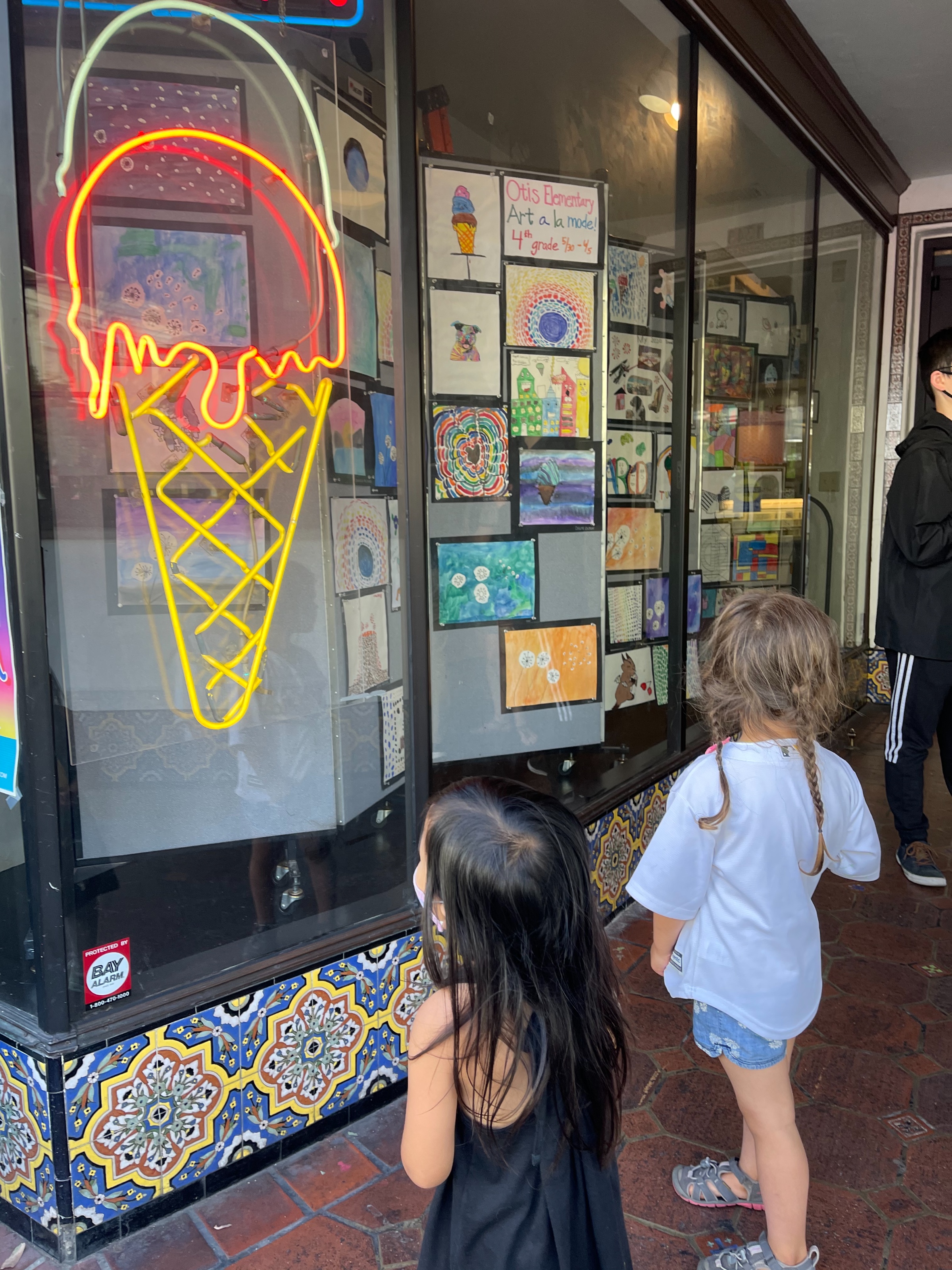 Two young children look at the neon lights shaped like ice cream, as they stand in front of Tucker's Ice Cream.
