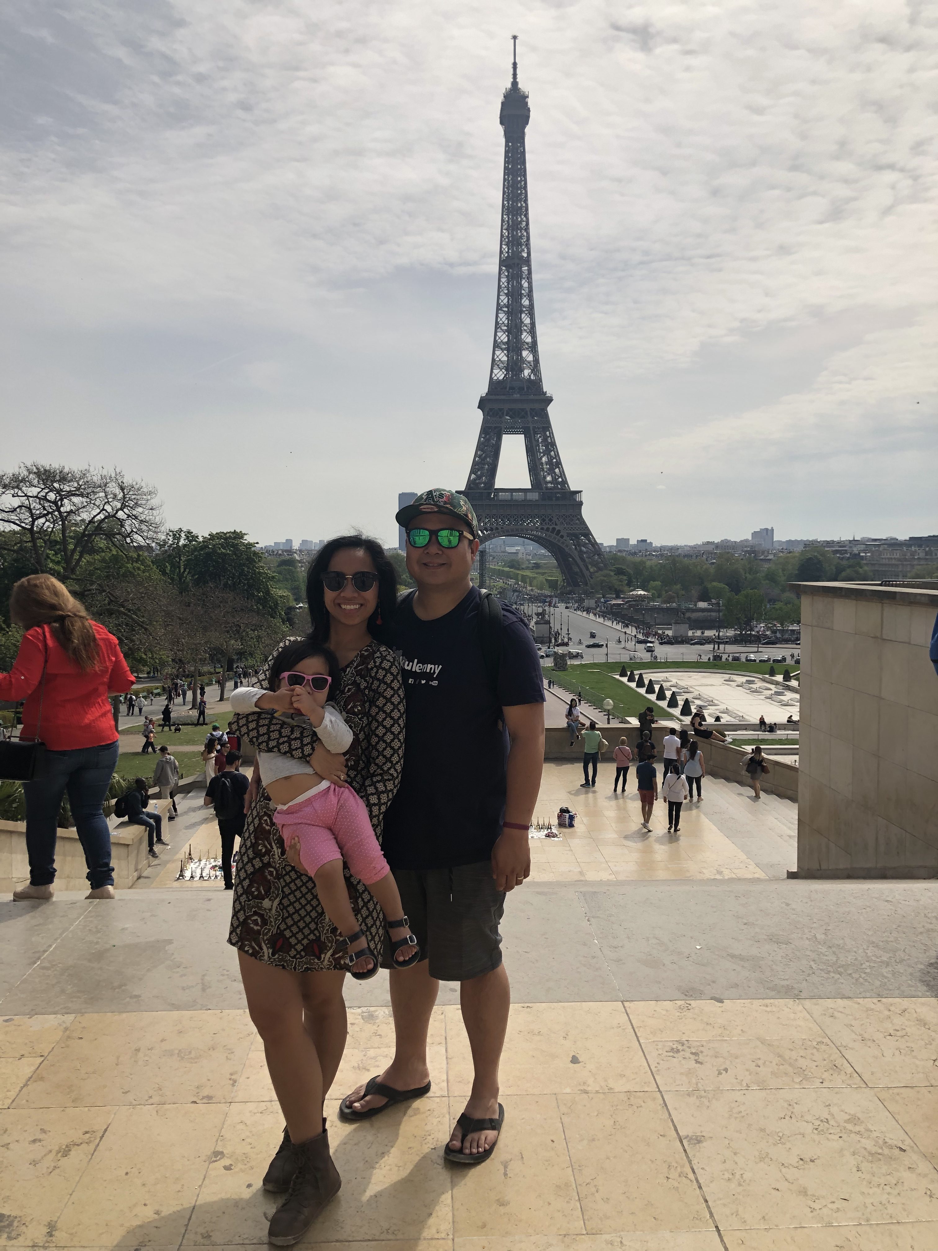 Angelica, standing next to her partner, holds her daughter. The Eiffel Tower can be seen in the background.