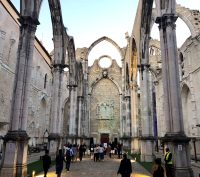 The stone columns of a gothic building with no roof impose above a crowd of visitors