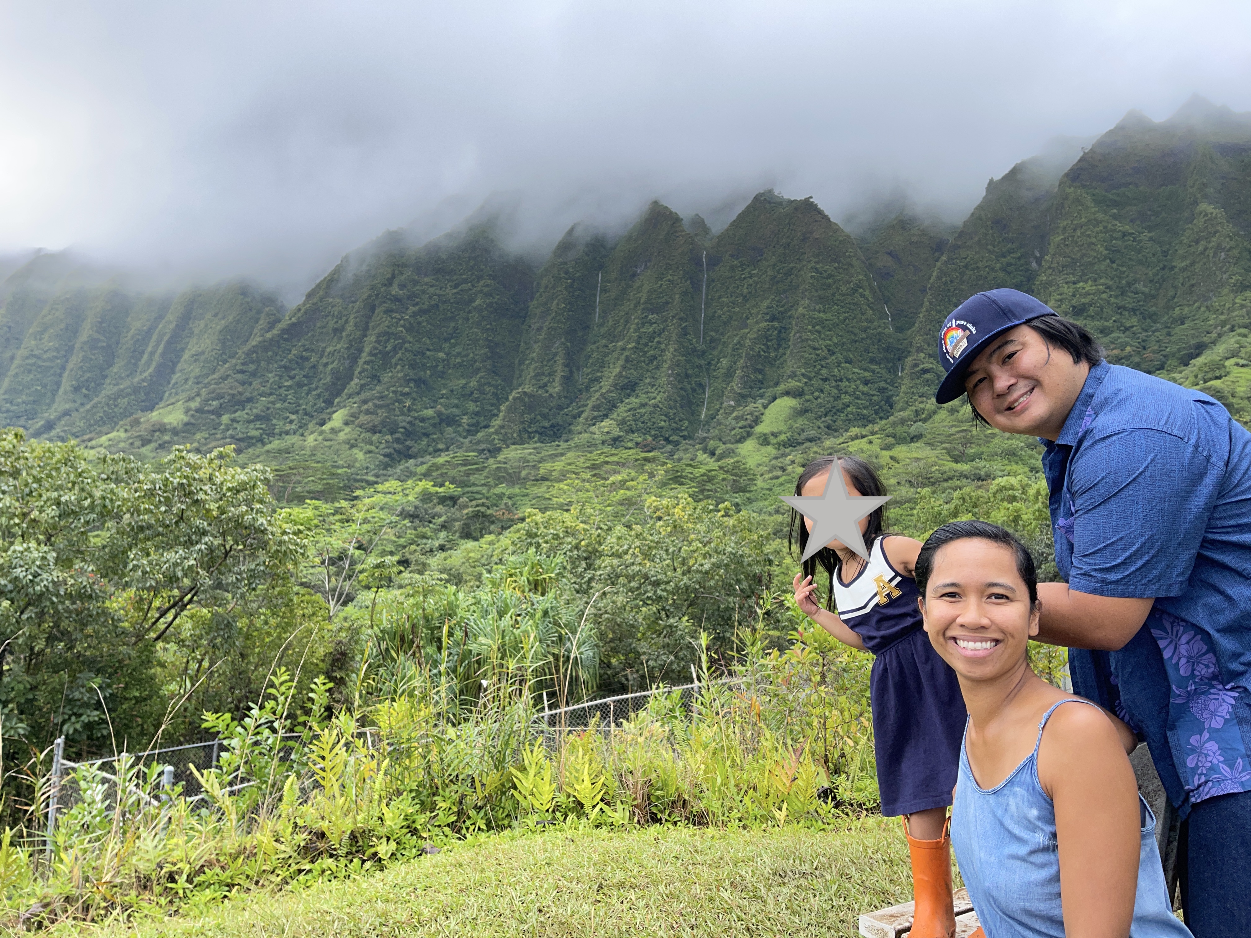 A family smiles at the camera against a backdrop of lush green mountains and mini waterfalls.
