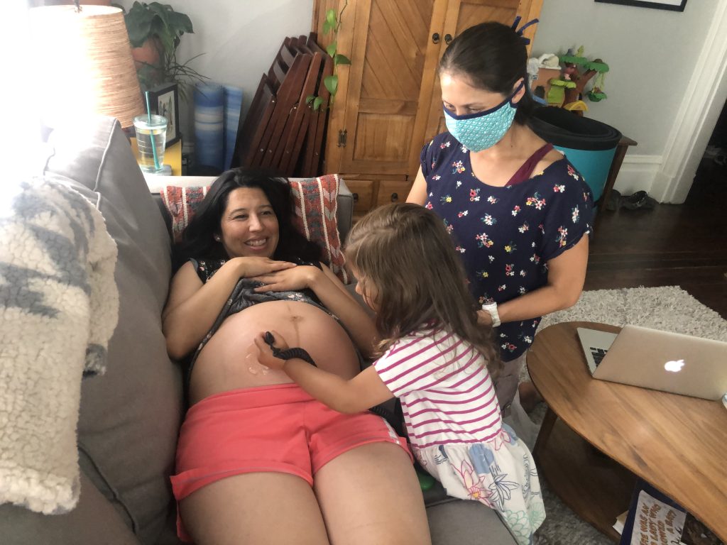 pregnant person checking baby heart rate at home with midwife and child