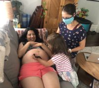 pregnant person checking baby heart rate at home with midwife and child