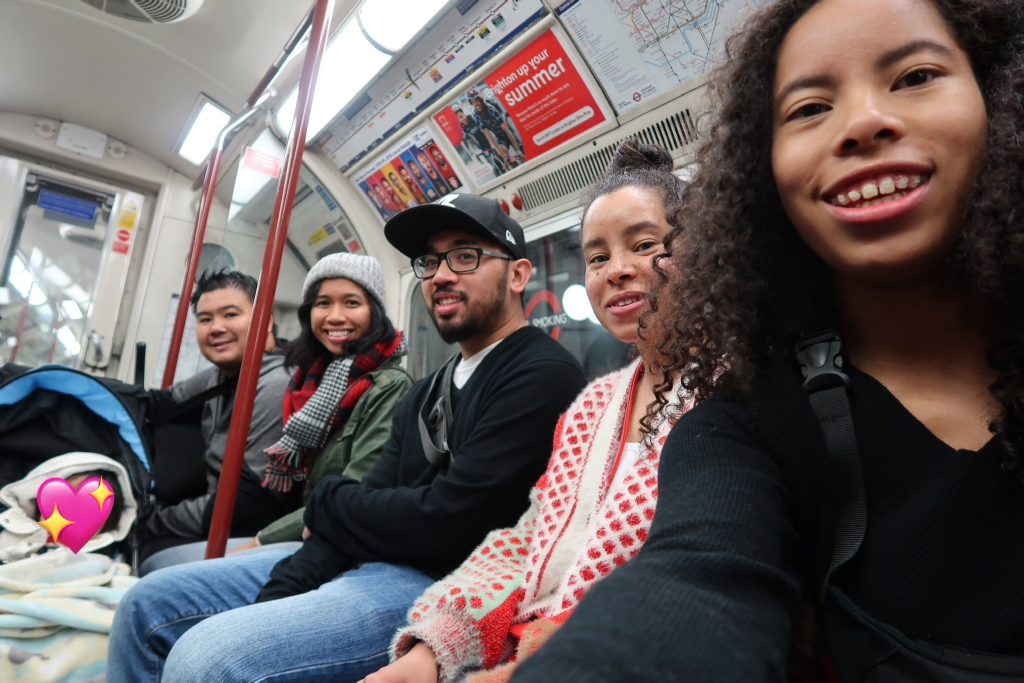 Angelica and five of her family members (including her child in a stroller) smile from their seats on the London Tube.