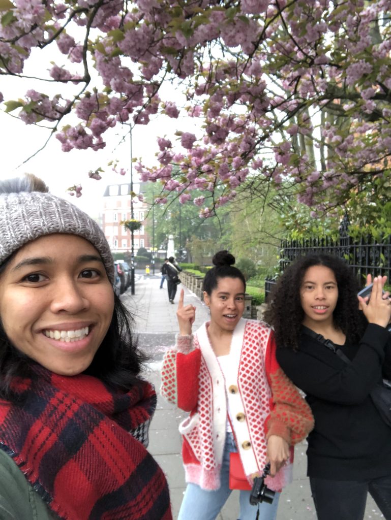 Angelica and two of her cousins smile under a pink-flowering tree in London.