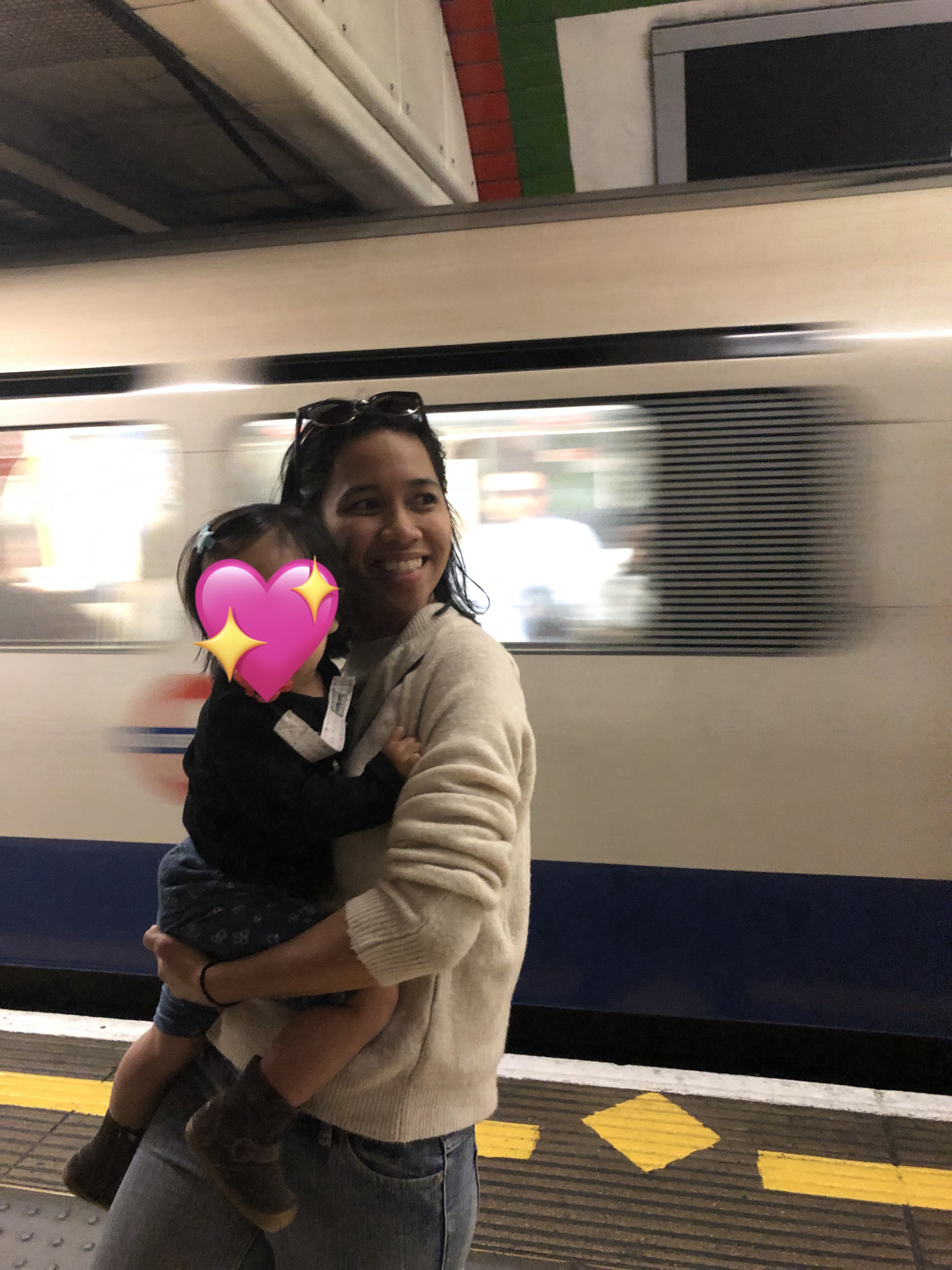 Holding her child, Angelica smiles in front of a passing train.