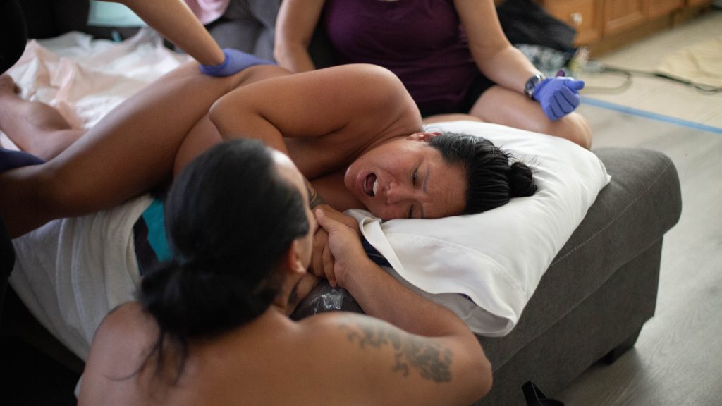 Person in labor being comforted by their partner and home birth midwife in Hawaii
