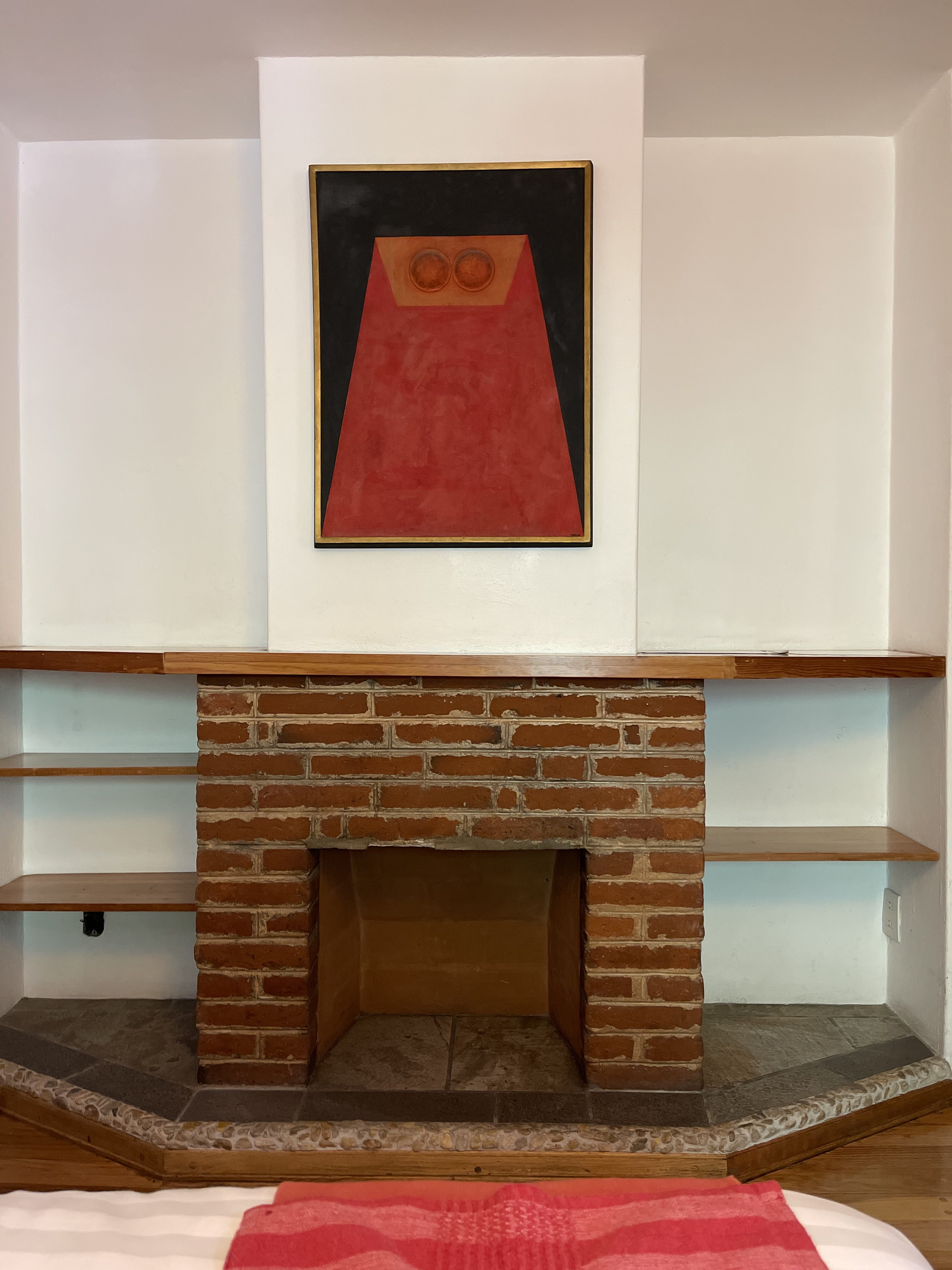 A red painting hangs above a fireplace.