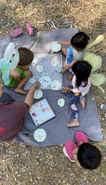 children dressed as fairies play a board game on a picnic blanket