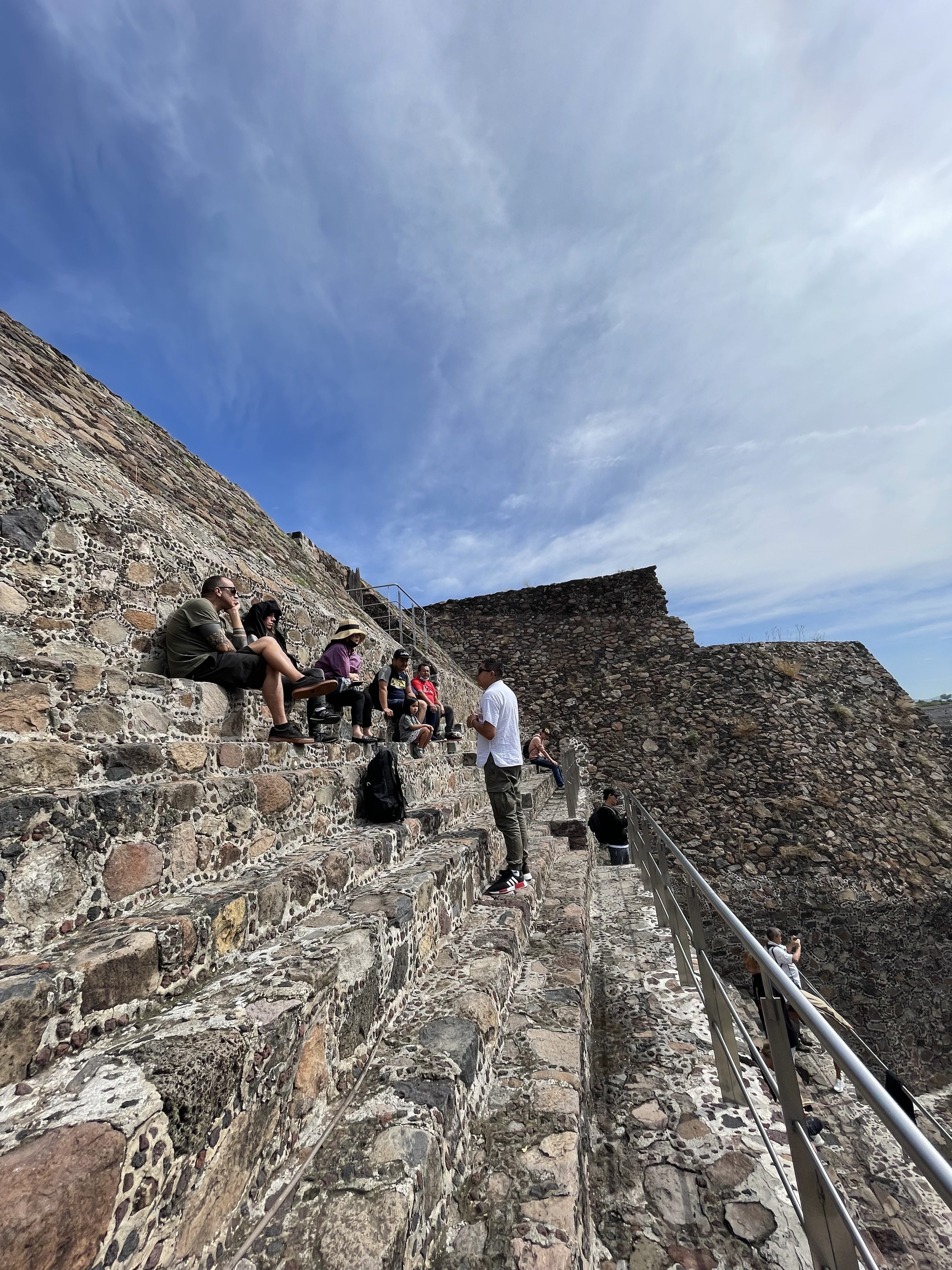 A tour groups listens to their guide as they face the Temple of Quetzalcoatl