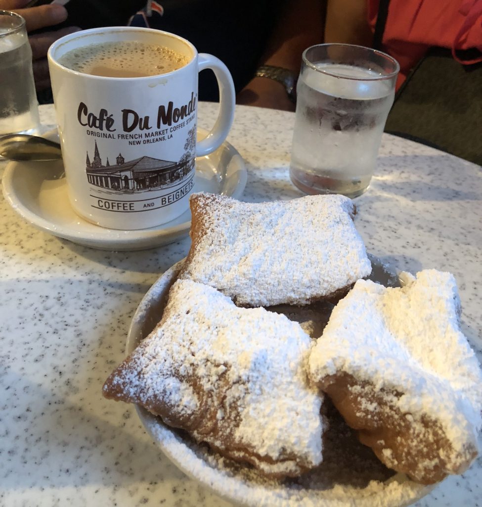 a plate of beignets covered in powdered sugar with a cup of coffee in the background