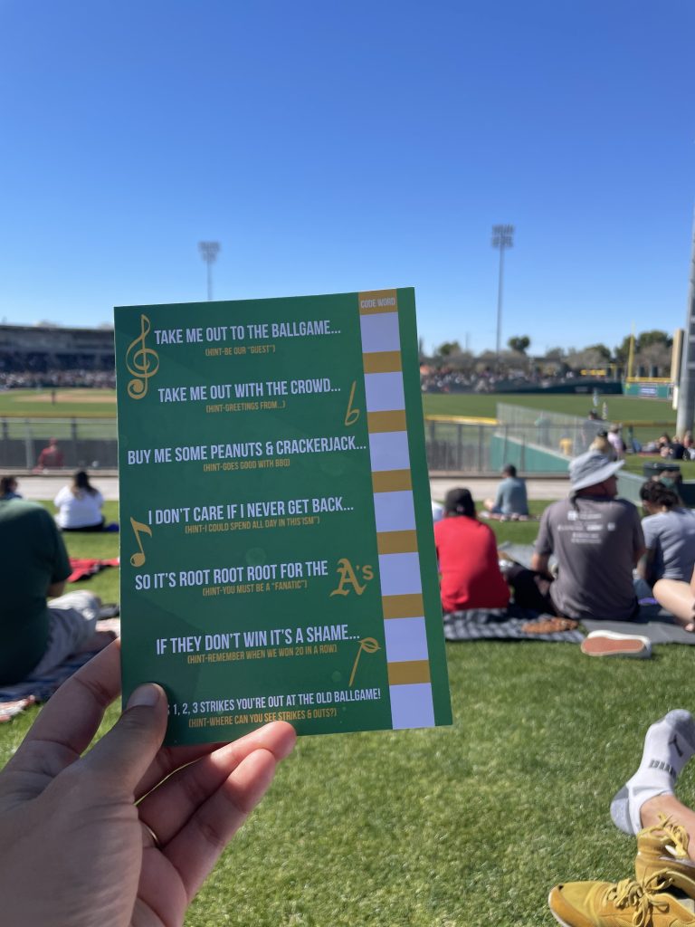 Hand holding up a scavenger hunt game in the outfield at Hohokam Stadium for the Oakland Athletics' Spring Training game
