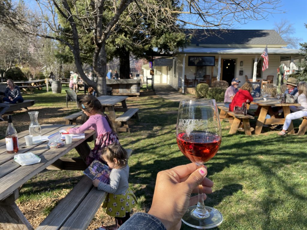 Glass of wine in a grassy area with two kids at a picnic table at Hovey Winery in Murphys on Main Street