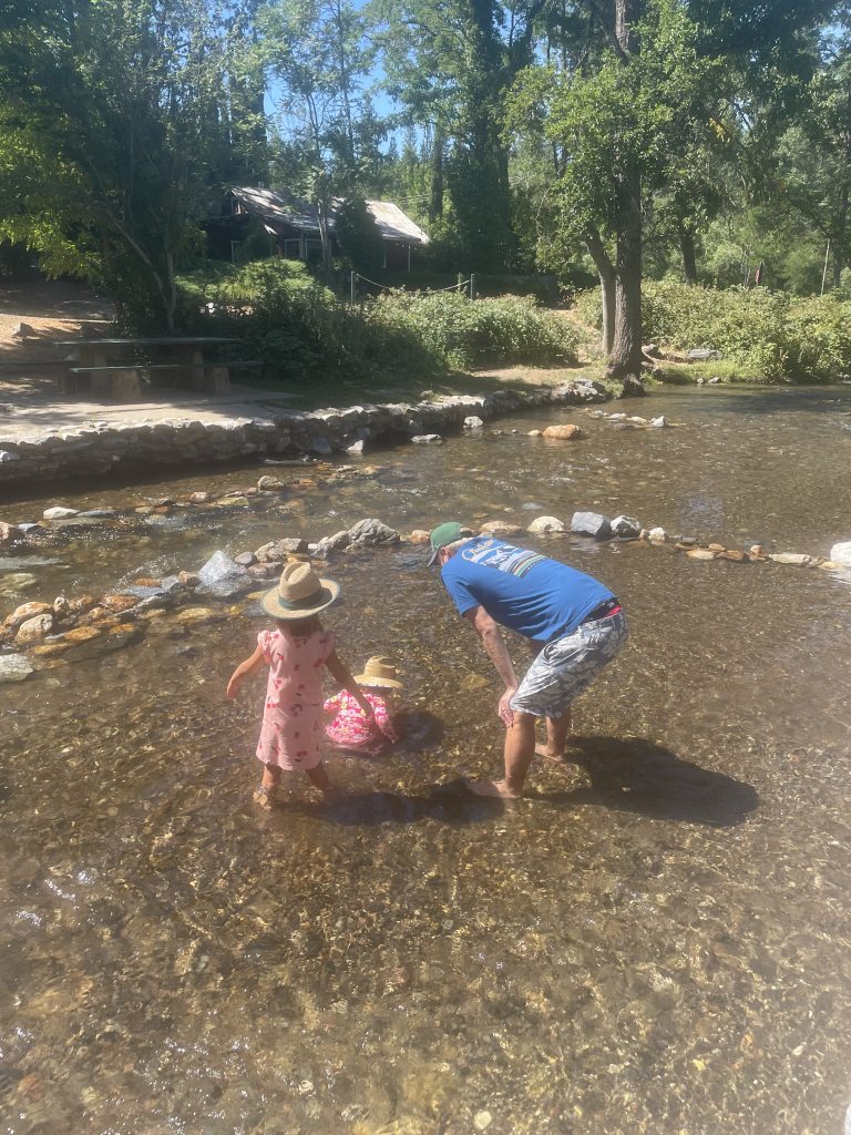 two children and an adult playing in a river flowing by Murphys Community Park