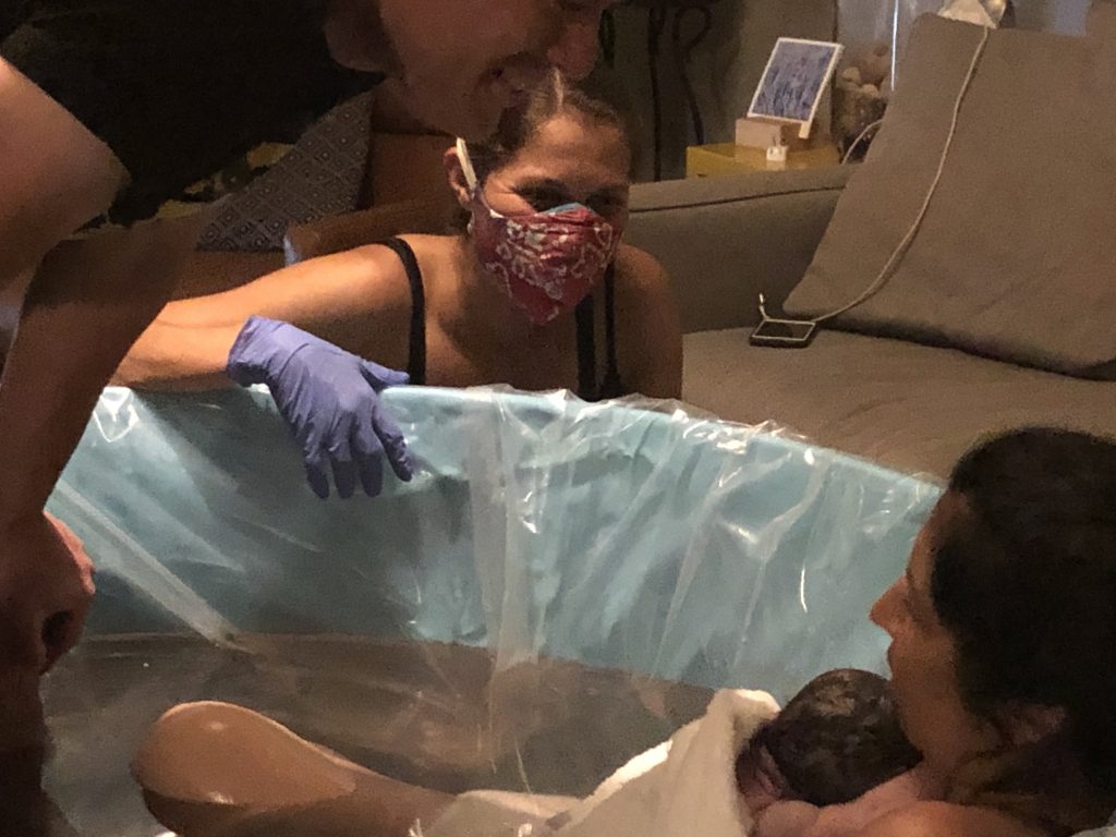 A midwife checking on a laboring person in a birthing tub after a water birth at home