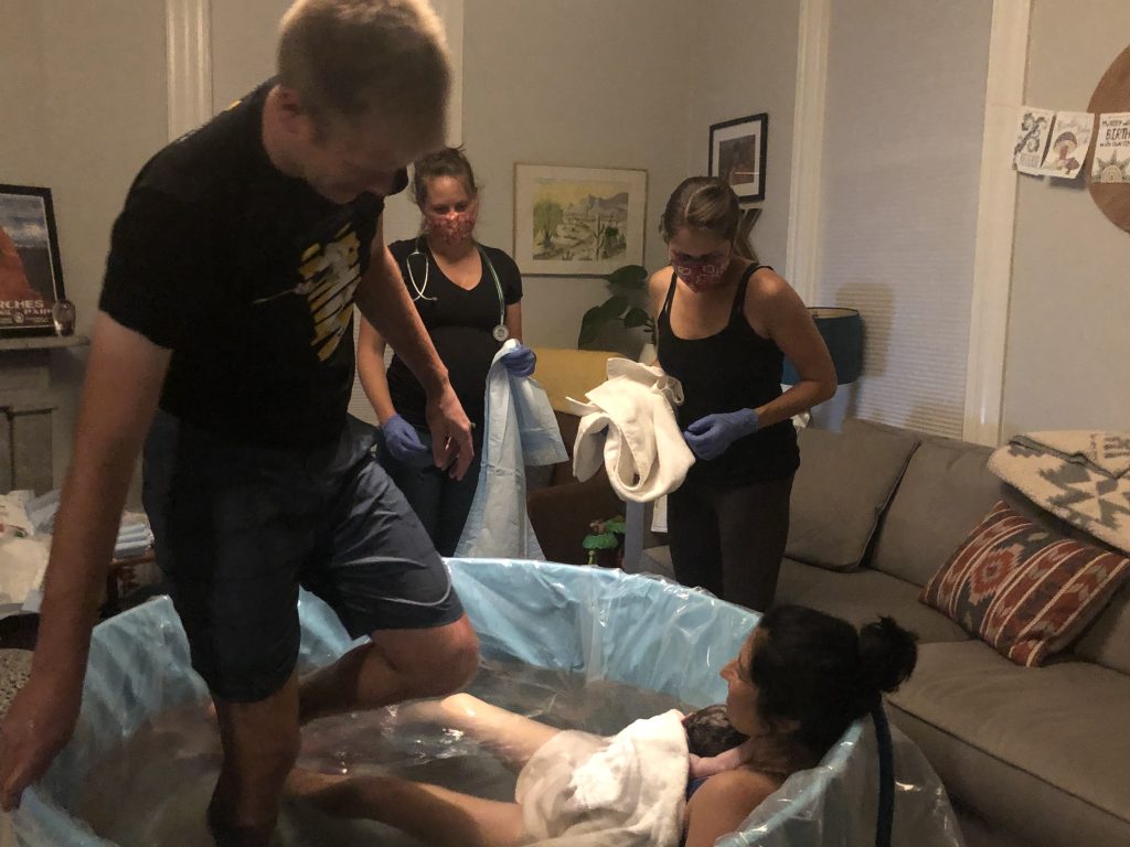 Laboring woman in tub after the baby was born surrounded by the homebirth team