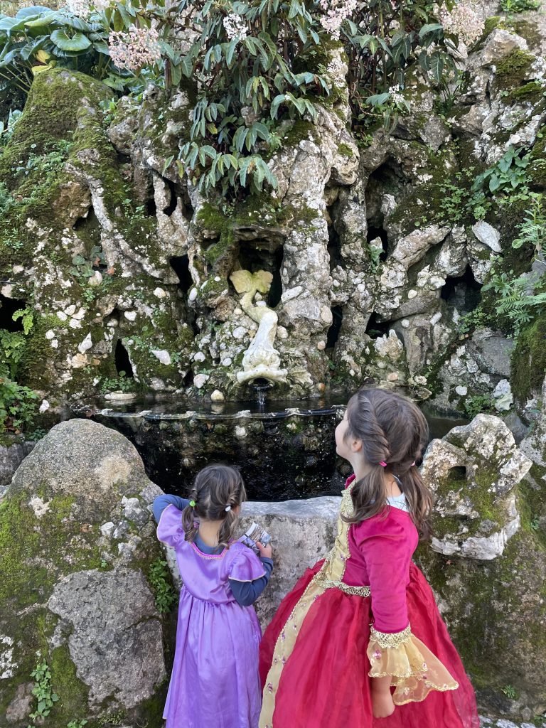 Two children in princess dresses gazing at a fountain at Quinta da Regaleira in Sintra, Portugal
