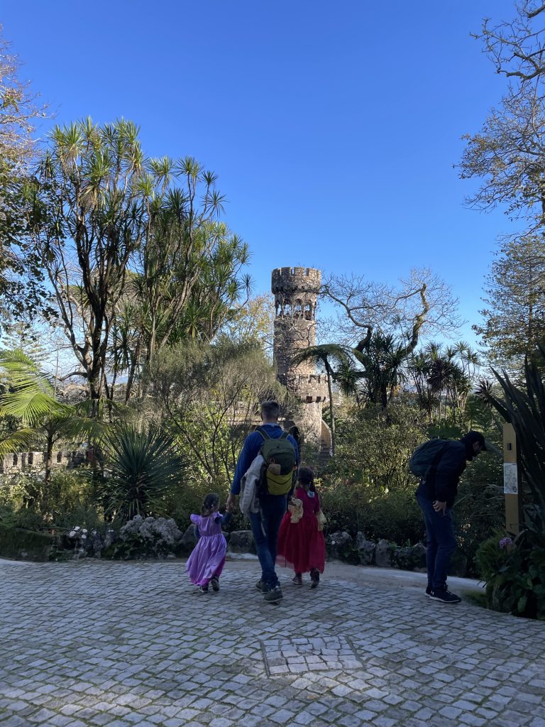 Parent with a child in each hand walking on a stone path at Quinta da Regaleira in Sintra Portugal