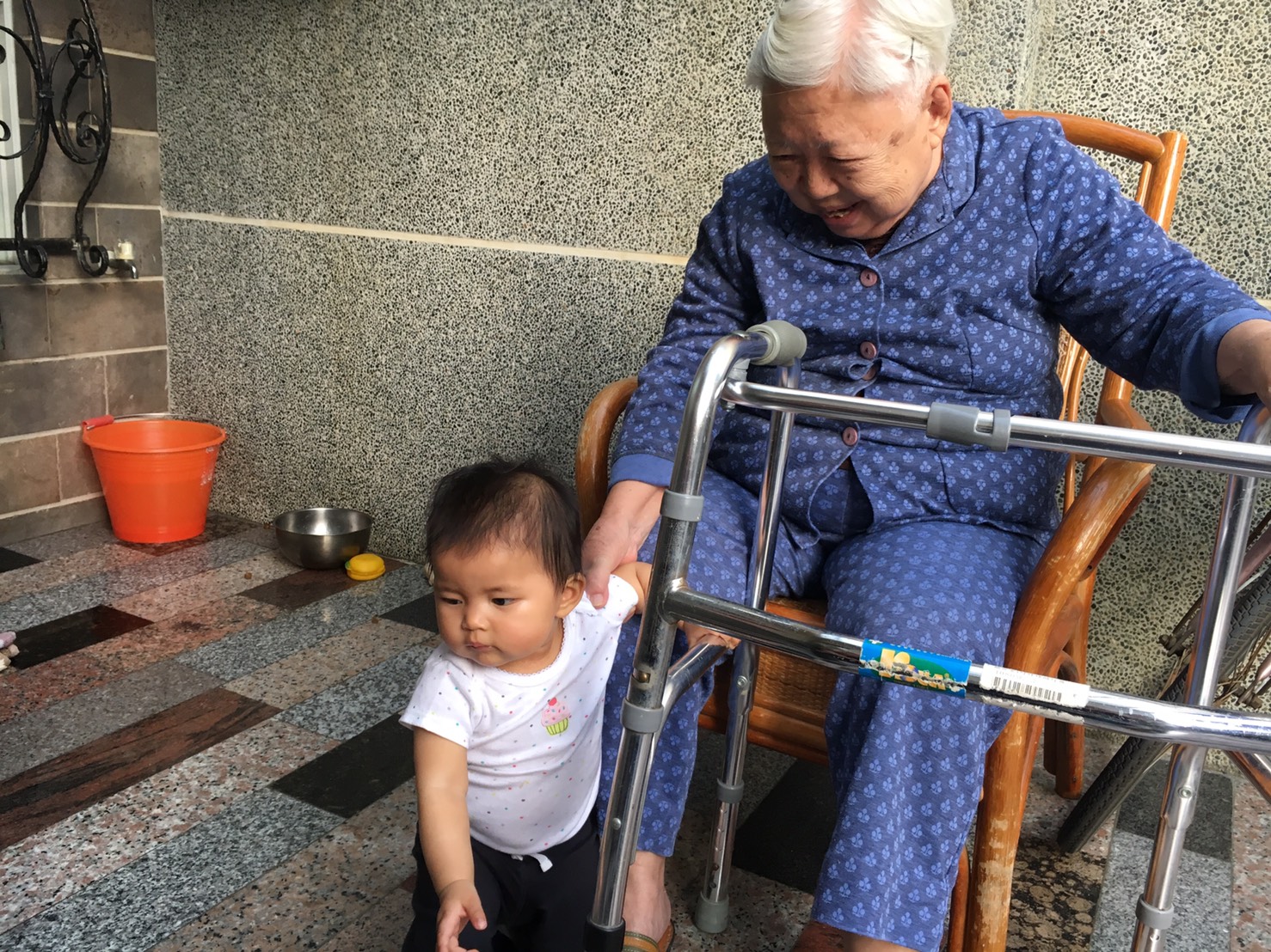 toddler next to her seated grandmother, wearing blue pajamas with a walker