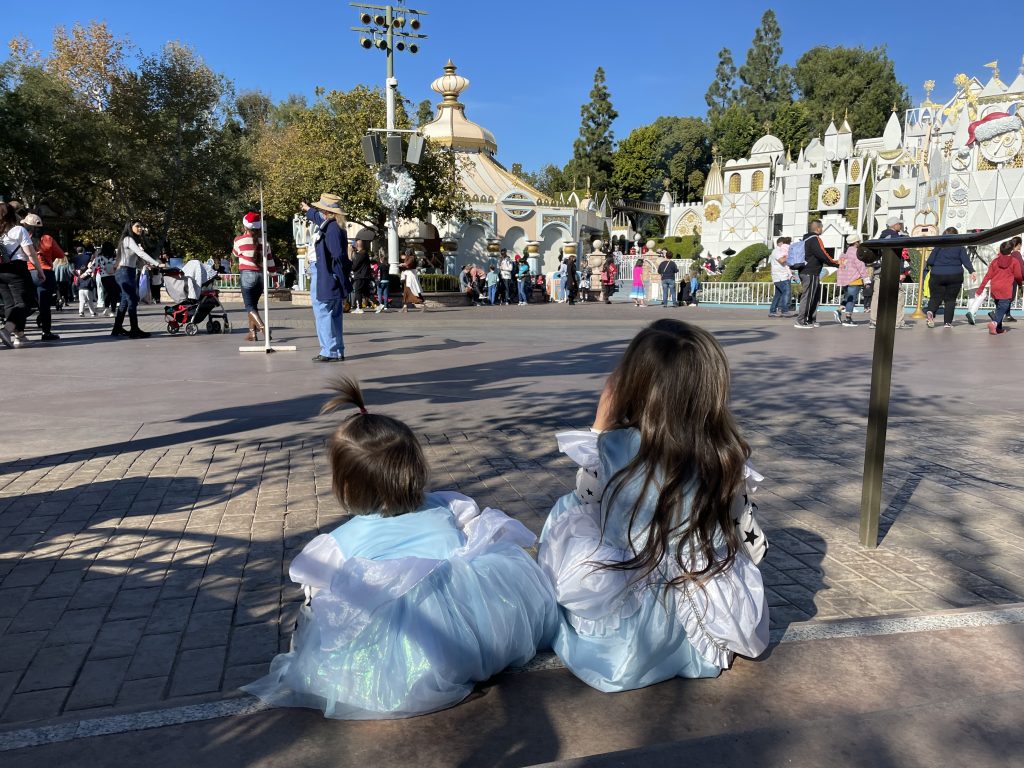 Two children dressed as Cinderella in Disneyland eating lunch near It's a Small World