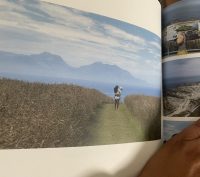 A hand holding a photo album of an adult walking with a child in Kaikoura New Zealand