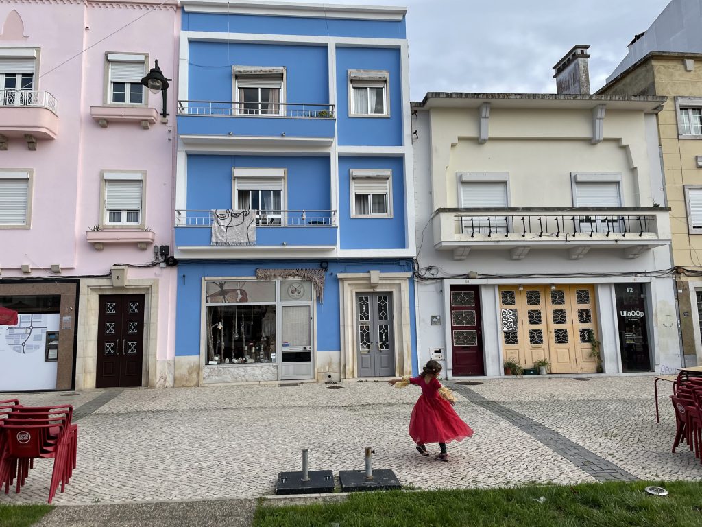 A child wearing a red princess dress in front of blue and pink painted buildings in Caldas da Rainha Portugal