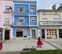 A child wearing a red princess dress in front of blue and pink painted buildings in Caldas da Rainha Portugal