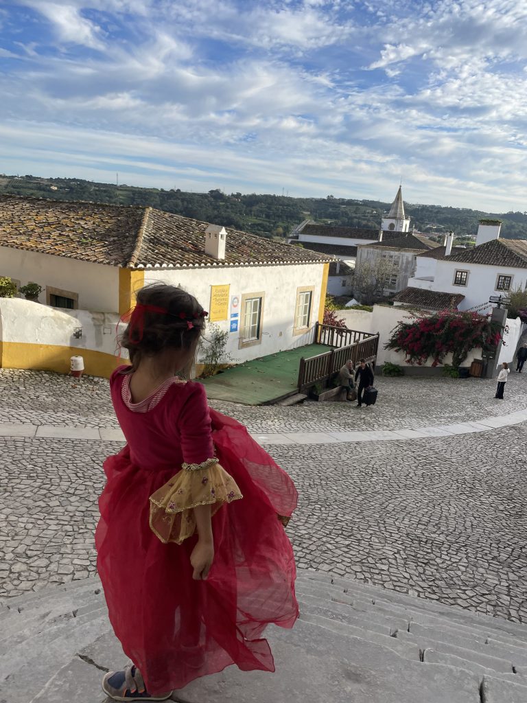 A child in a red princess dress looking at Rua Direta in Obidos Portugal