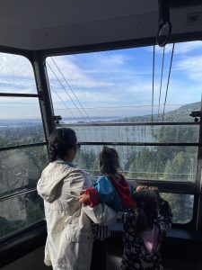 An adult and two children looking at the view of blue skies and green mountainside from the gondola up to Grouse Mountain in Vancouver BC