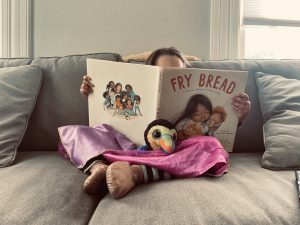 A child reading the book Fry Bread on a sofa in a pink princess dress