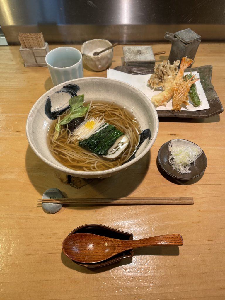 A full Japanese meal of noodle soup, tempura, and various utensils and spice bowls, as seen from above.