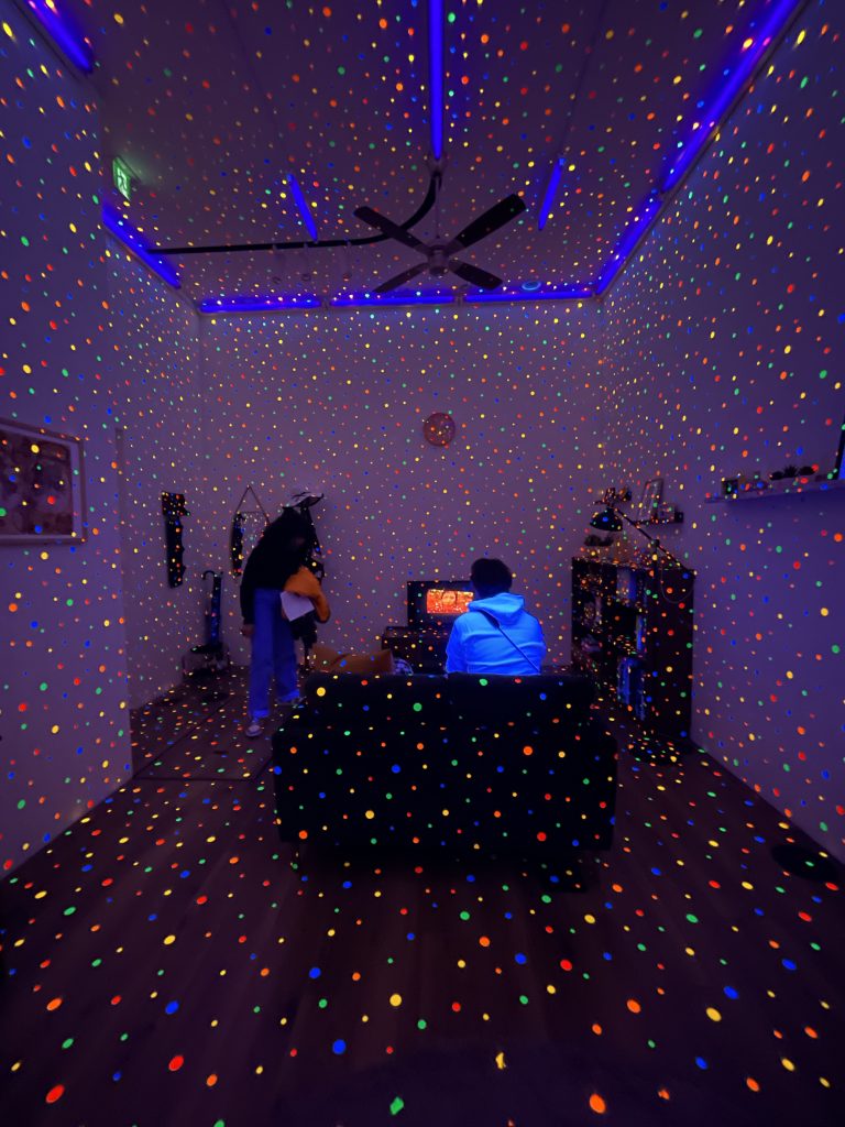 People sit in a dark, purple-hued room that is decorated with bright glow-in-the-dark dots.