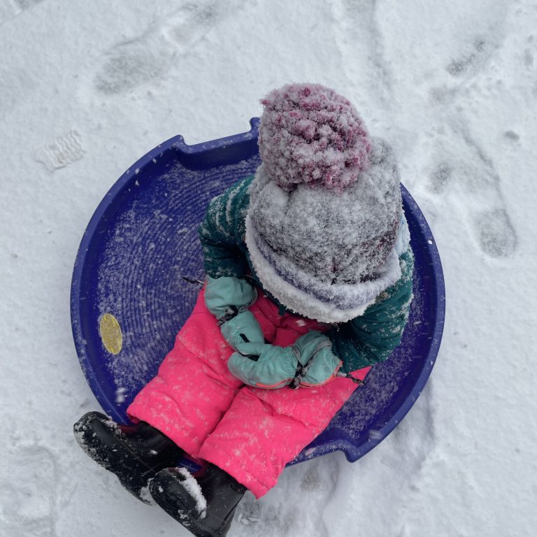 A child sitting on a round sled with gloves at Calaveras Big Trees State Park in winter